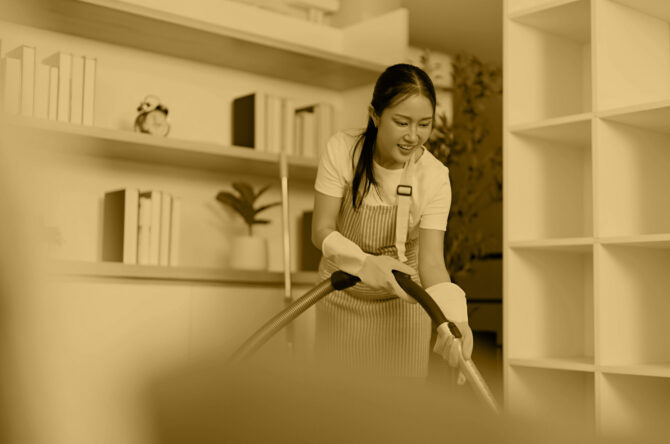 A cheerful woman enjoys cleaning her home with a vacuum cleaner, wearing gloves and headphones, embodying a positive cleaning routine.